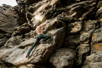 Rock climber climbs bouldering on a cliff on forest. Low angle of strong rock climbing man hanging free on rock with sunflare
