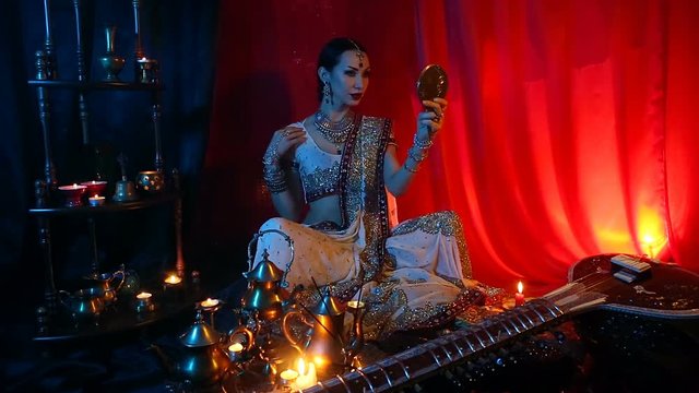 Beautiful young indian woman in traditional Sari clothing with Oriental Jewelry looking in the mirror and trying on jewelry