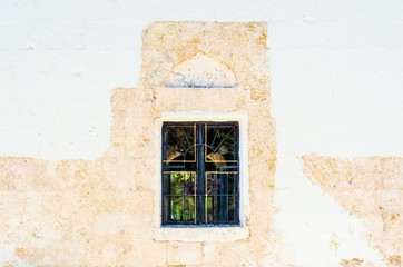 A window of a medieval monastery in Greece. Knights' heritage in Rhodes. Background with a white and beige wall with a dark window 