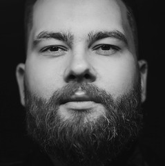 Obraz premium Black and white image of handsome bearded man in black over black background 