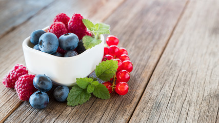 Culinary berry creation in small porcelain dessert bowl arranged on wooden table and lemon balm decoration, with space for text