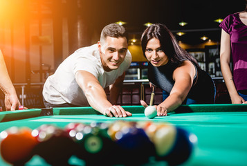Group of young cheerful friends playing billiards.