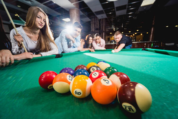 Group of young cheerful friends playing billiards.