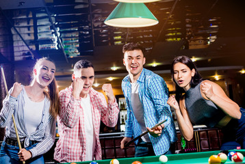 Group of young cheerful friends playing billiards.