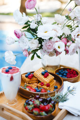 Obraz na płótnie Canvas breakfast by the pool with fruits and berries in wooden bowls: waffles, milkshake, strawberries, raspberries, blueberries, cherries, orange slices, lemon, lime, watermelon and pineapple