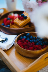 breakfast by the pool with fruits and berries in wooden bowls: waffles, milkshake, strawberries, raspberries, blueberries, cherries, orange slices, lemon, lime, watermelon and pineapple