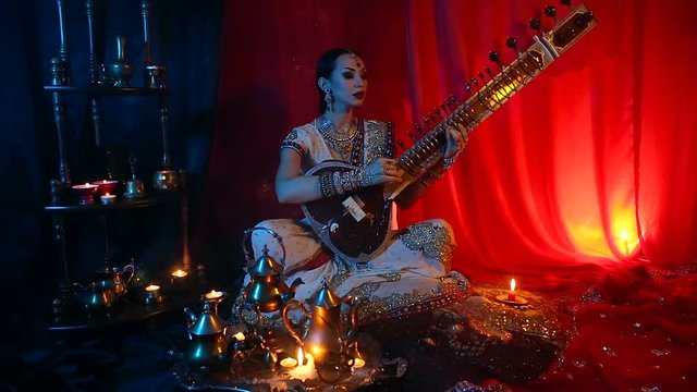 Beautiful young indian woman in traditional Sari clothing with Oriental Jewelry Playing the Sitar.