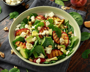 Summer Peach Salad with spinach, avocado, walnuts and feta cheese in rustic bowl. healthy food.