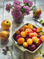Fruit set of fresh fruits in a ceramic plate, a bouquet of forest carnations in a small vase
