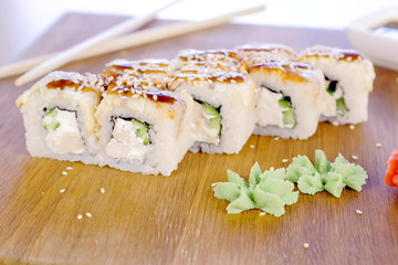Rolls with fish and sesame seed on top served in wooden board with wasabi, ginger and soy sause