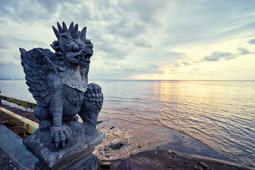 Art and travel. Hindu stone statue of demon on the sea shore with beautiful sunset view.