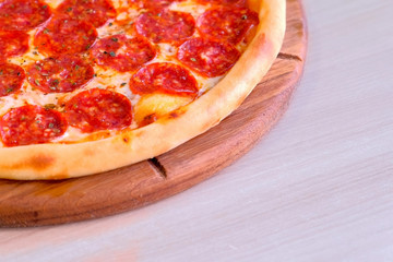 Quarter of salami pizza on wooden board on the table. Close-up view
