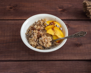 Breakfast of oatmeal with nectarines and cinnamon in a deep plate, served on a wooden table