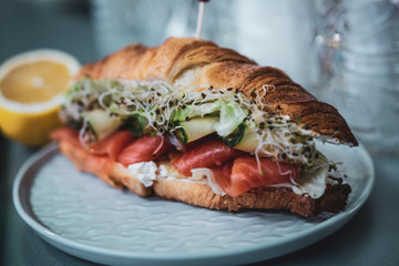 Sandwich with salmon, microgreen, cucumber in croissants, on the table