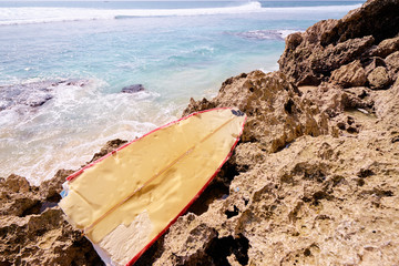 Half of a broken vanilla-red surfboard left behind on a dead rift remains on the beach.