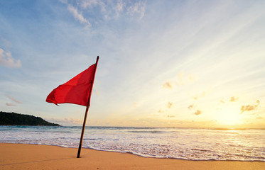 Beautiful sunset on tropical sand beach with red rescue flag.