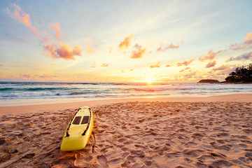 Beautiful landscape. Sunset on the sea beach with lifeguard surf board on sand.