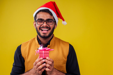 indian man wearing stylish traditional kurta great smile in santa hat with gift box on yellow background studio.dark-skinned Santa Claus congratulating merry christmas