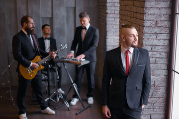 Music band and fashion.  Handsome young men in suits with instruments indoors.