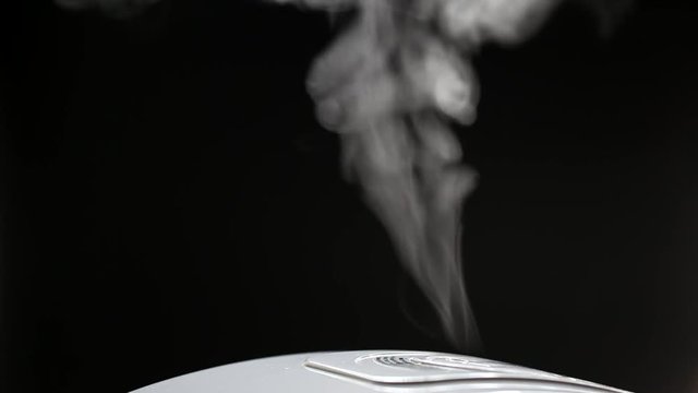 Smoke rising from electronic rice cooker in the kitchen on dark background