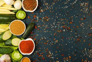 THE VEGETABLES ON THE STONE A DARK BACKGROUND. YOUNG HERBS ONIONS GARLIC GREEN BEANS YELLOW CORN ZUCCHINI SPICES ARE BRIGHT ON A DARK TEXTURED BACKGROUND.