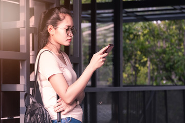 Copy space and flare. Asian girl wearing glasses standing using smartphone in the building shade. And the sunlight on.