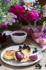 Breakfast of quark pancakes, black currant custard, currants and a bouquet of wild flowers on a wooden background.