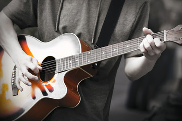 Fototapeta premium A professional musician plays an improvised melody on a six-string acoustic beautiful guitar, holding a mediator in his hand. Photo in black and white to highlight the brightness of the music