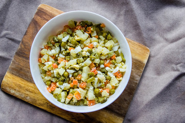 Russian salad Olivier with potato carrot green peas on the board and gray background