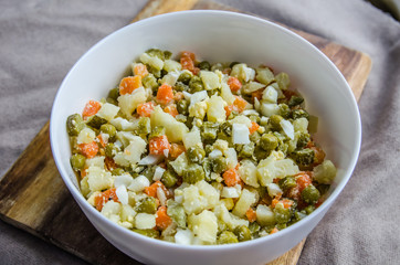 Russian salad Olivier with potato carrot green peas on the board and gray background