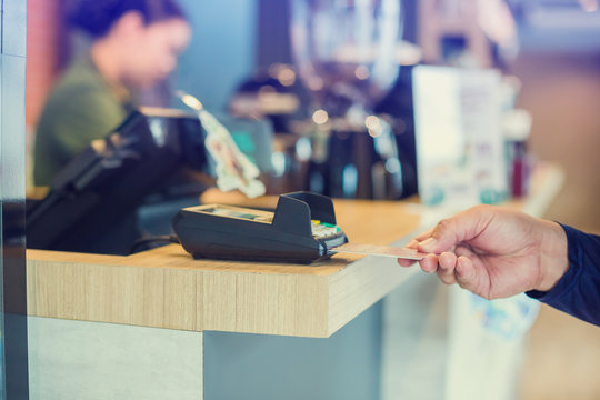 Hand put credit card In slot of credit card reader with blurry cashier at counter service, credit card payment, buy and sell products & service, the concept of payment without cash, selective focus.