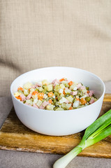 Russian salad Olivier with potato carrot green peas ham on the board and gray background