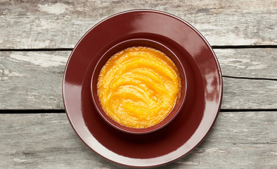 Pumpkin cream soup or porridge in a bowl on wooden rustic background from above, flat lay, overhead top view, closeup, autumn harvest food and holiday halloween or thanksgiving concept