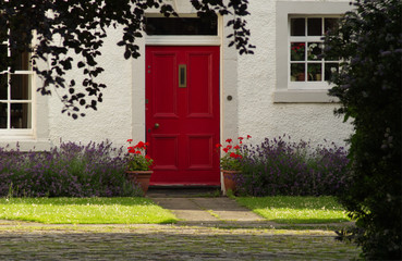 A lovely Scottish cottage with a red door and lavender growing next to a green lawn