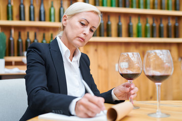 Experienced winery expert making notes about characteristics of red wine