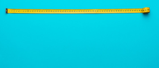 Top view of yellow soft measuring tape. Minimalist flat lay image of tape measure with metric scale over turquoise blue background with copy space.