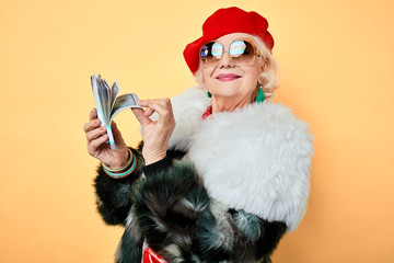 happy old stylish woman in sunglasses boasting her money. isolated yellow background, studio shot,...