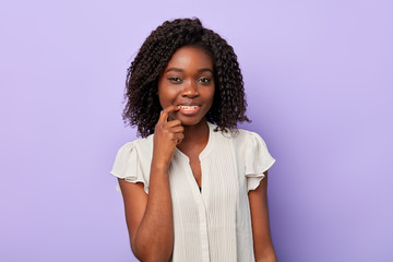 Fototapeta na wymiar Portrait of a young happy afro woman pointing to her teeth isolated blue background. puzzled smiling girl with a finger on her lips looking at the camera . idea, plan concept
