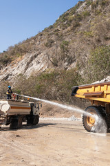 Male worker on water truck is spraying water on the large wheel truck. © Tanes