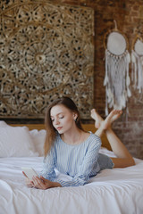 Fototapeta premium Young sweet girl lying on bed with phone