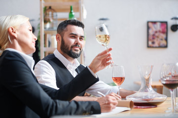 Young successful cavist looking at white wine held by his colleague