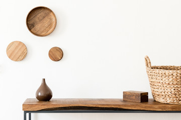 Design scandinavian interior of living room with wooden console, rings on the wall, vase, rattan basket and elegant accessories. Stylish composition of home interior. Home decor. Template. Copy space.