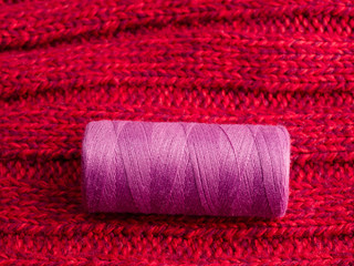 Sewing still life magenta spool of thread on background of red wool fabric