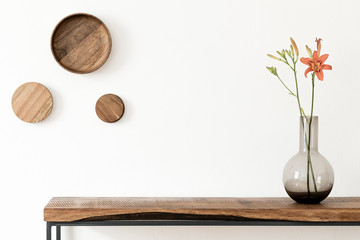 Stylish and modern scandinavian room interior with wooden console and rings on the wall, flowers in brown vase. Design composition of home interior. White walls, copy space. Home decor. Template.