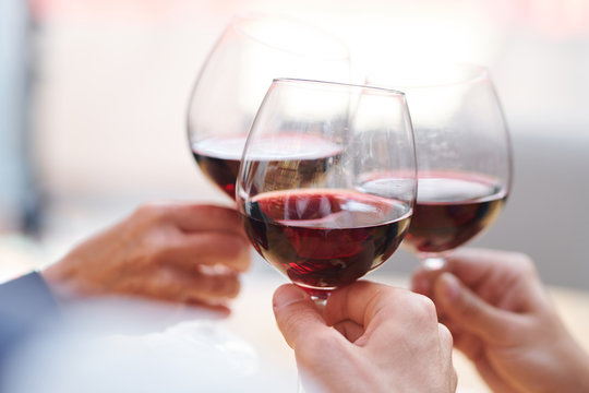Three wineglasses with red cabernet held by group of toasting friends