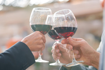Hands of friends or business partners clinking with wineglasses with red wine