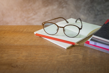 Blank open book with red pencil and glasses  on the wooden table. cement wall background, copy space.