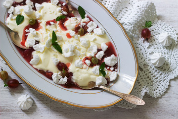 Eton mess, traditional English dessert with gooseberry, whipped cream and meringue on a light background. Rustic style.