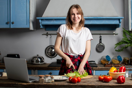 young girl prepares a vegetarian salad in the kitchen and looks into a laptop, she learns to cook by a video tutorial, preparing healthy food