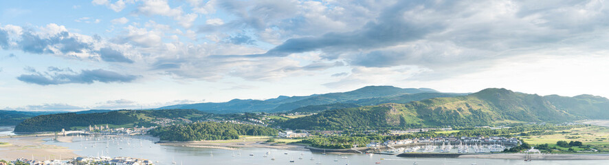 Fototapeta na wymiar Panoramic North Wales vista over the Conwy estuary nestled below the Welsh mountains. Conwy castle and marina bathed in beautiful evening light.